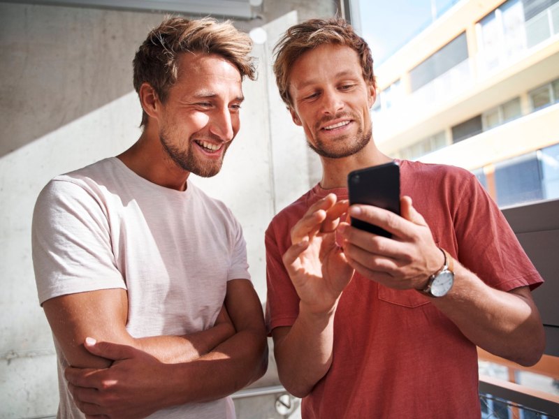 Ein Mann zeigt einem anderem Mann etwas auf seinem Handy.
