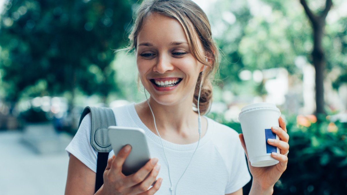 Frau mit Kopfhörern schaut aufs Handy.