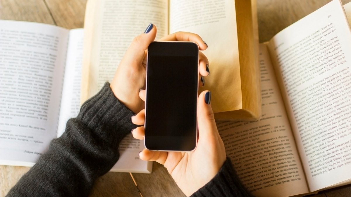 Hand hält iPhone über Büchern