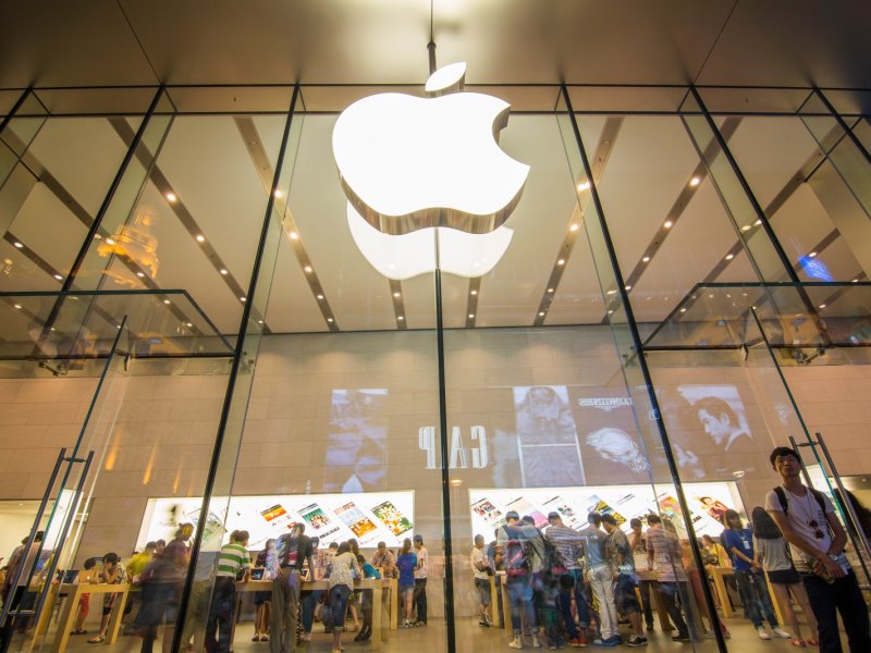 Apple-Store von vorne mit dem berühmten abgebissenen Apfel als Logo und Besuchern in Hintergrund.