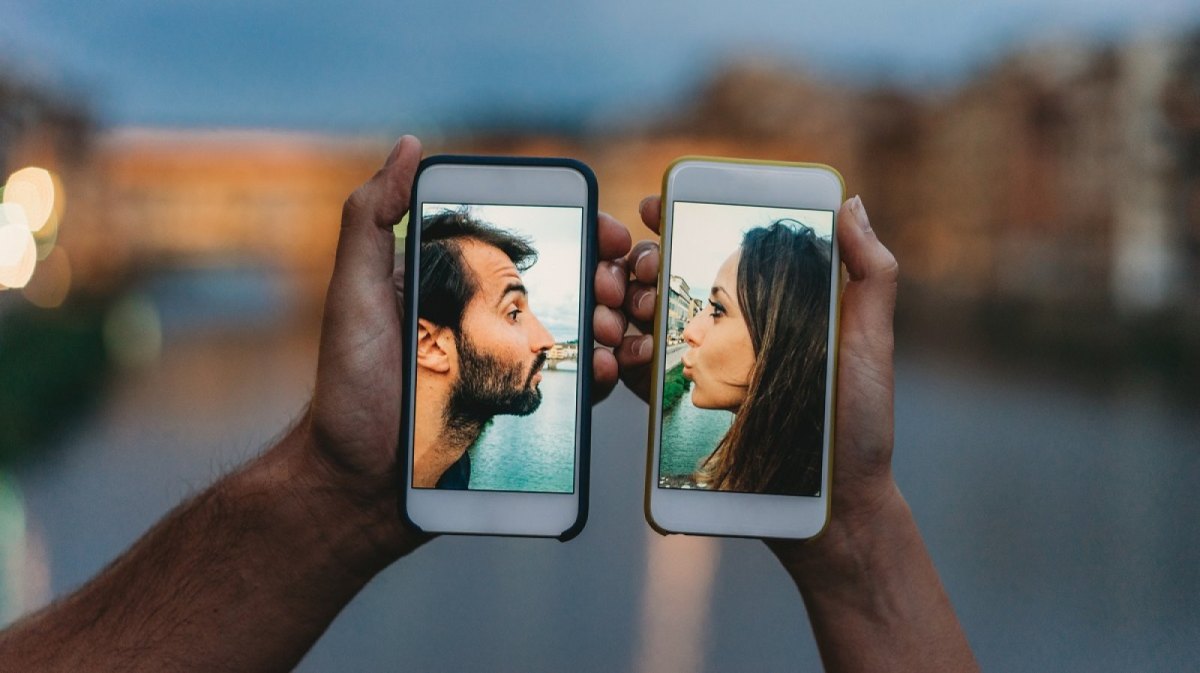 Pärchen küsst sich über ein Handy.