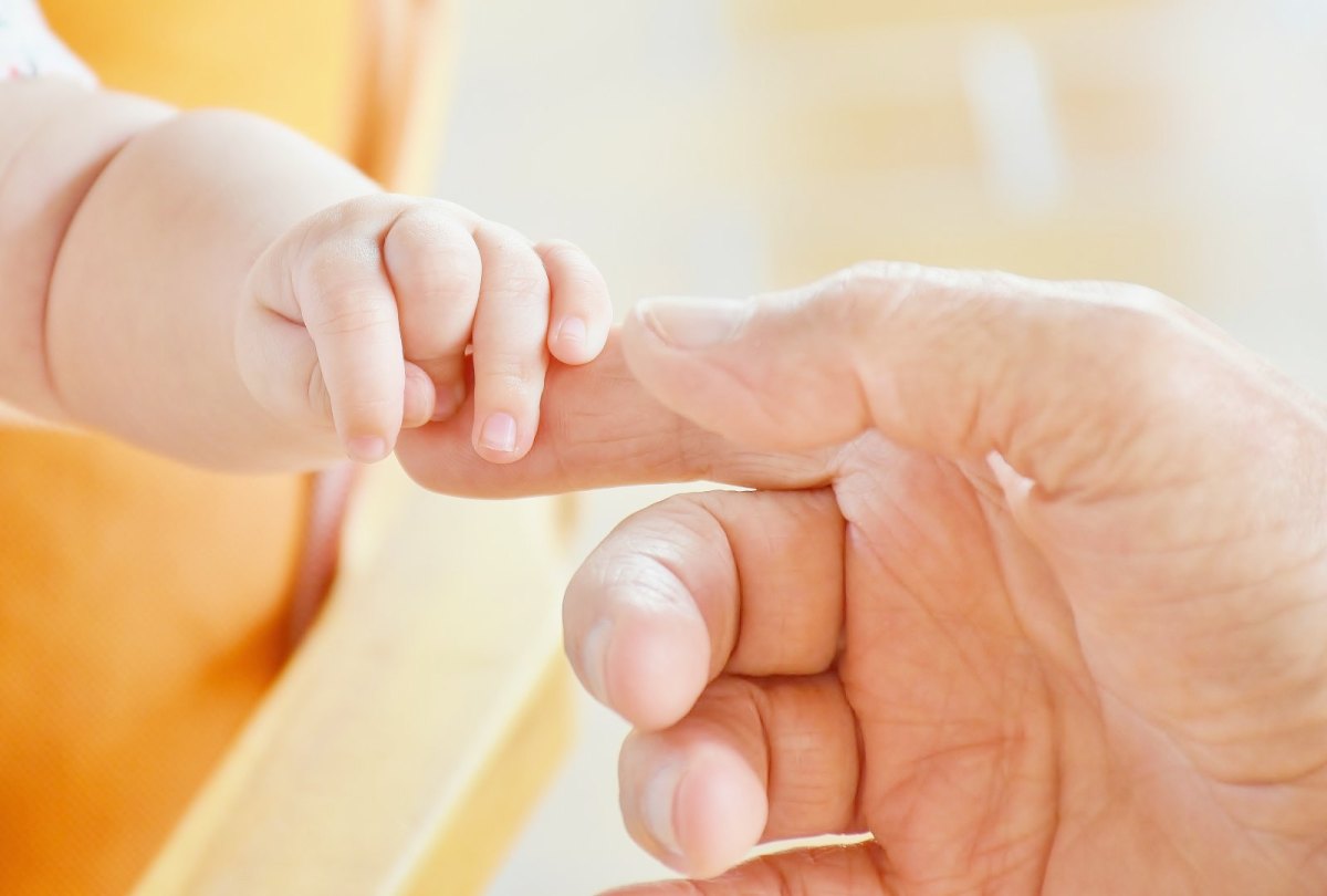 Hand eines Erwachsenen greift Fuß eines Babys.