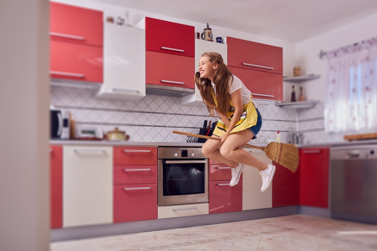 Frau fliegt auf Besen durch die Küche.