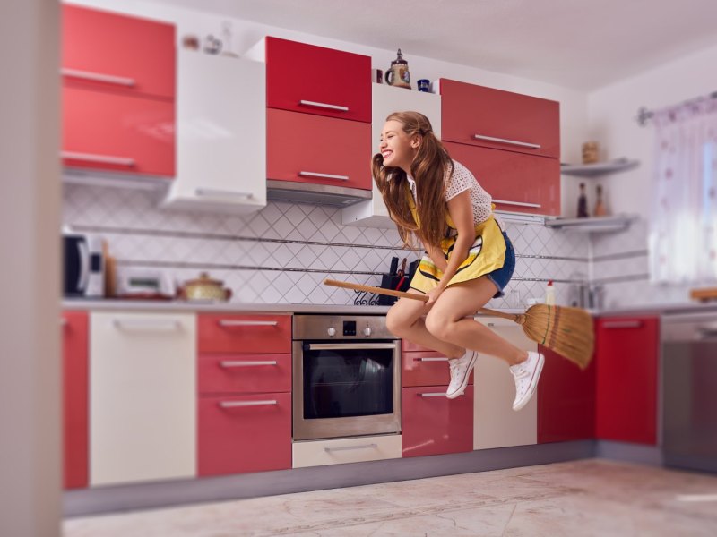 Frau fliegt auf Besen durch die Küche.