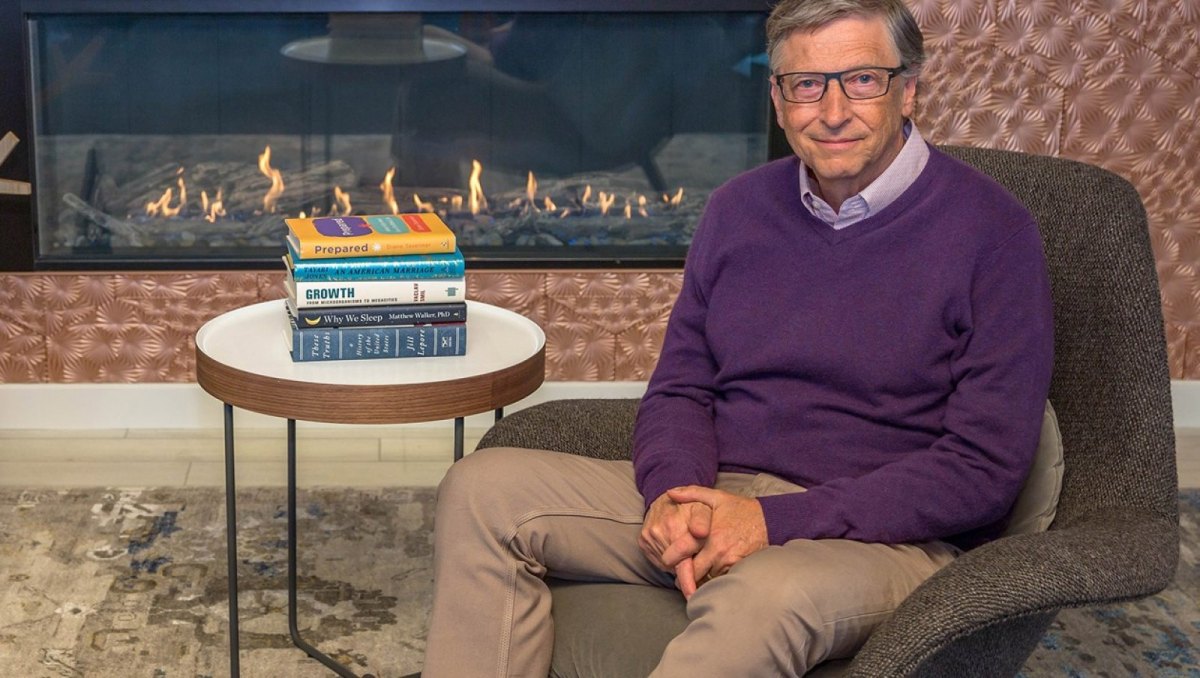 Bill Gates mit Büchern vorm Kamin.