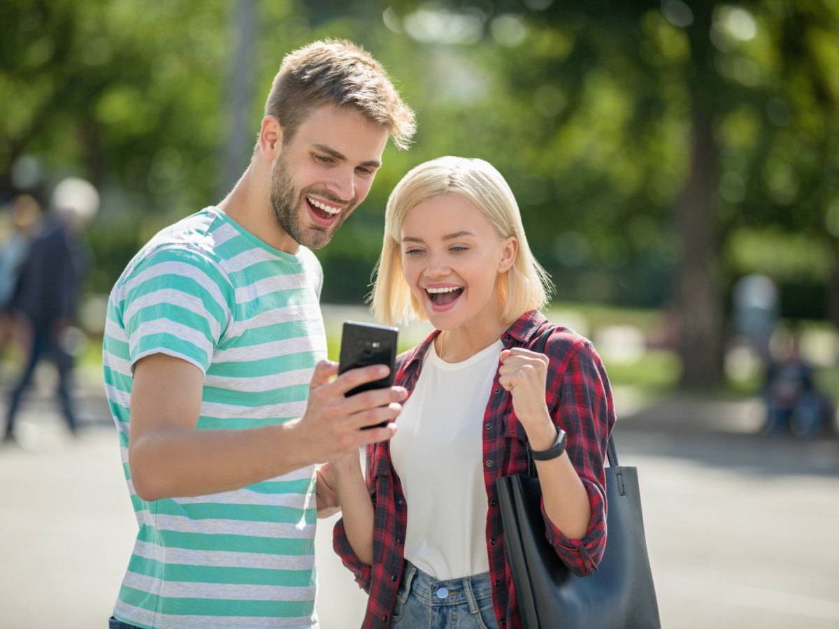 Ein Mann und eine Frau blicken auf ein Handy und freuen sich.