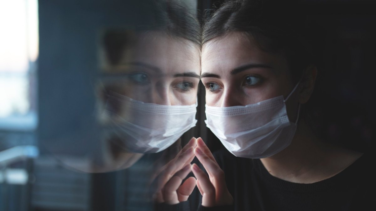 Frau mit Maske spiegelt sich im Fenster