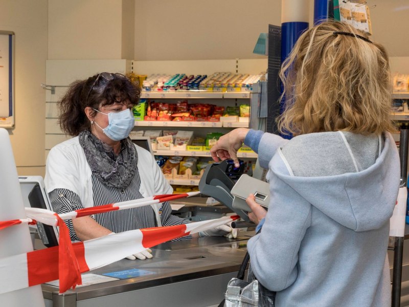 Eine Frau bezahlt mit Karte in einem Geschäft. Eine Kassiererin mit Mundschutzt sitzt vor ihr.