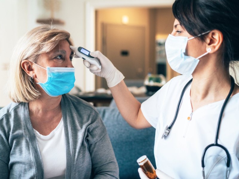 Ärztin mit Mundschutz misst Fieber bei einer Patientin an der Stirn.