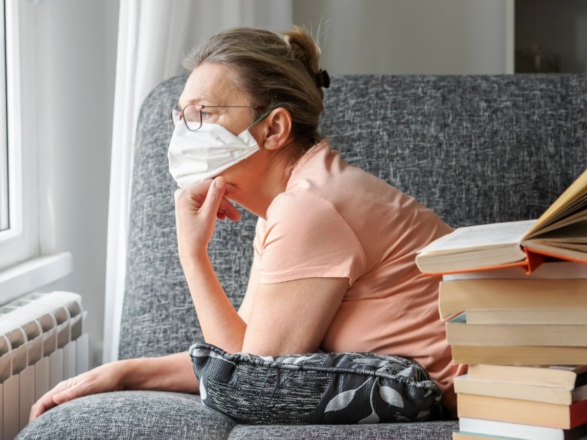 Frau blickt mit Mundschutz aus dem Fenster.
