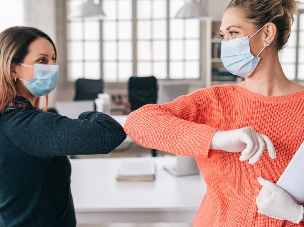 Zwei Frauen mit Mundschutz begrüßen sich mit den Ellenbogen.