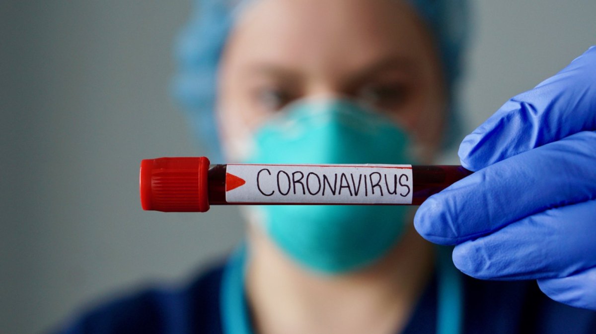 Ärztin hält Blutprobe mit der Aufschrift "Coronavirus" in die Luft