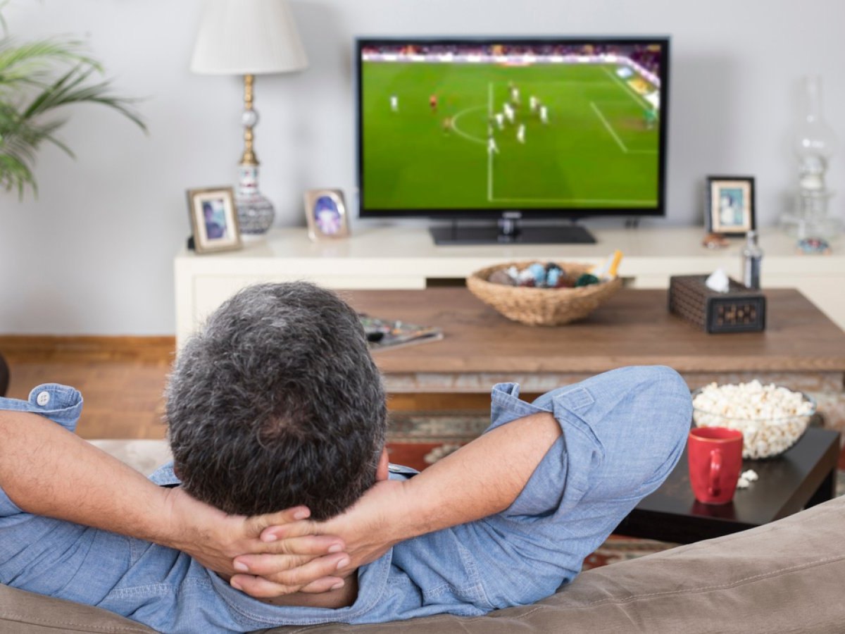 Mann sitzt vor dem TV und schaut Fußball.