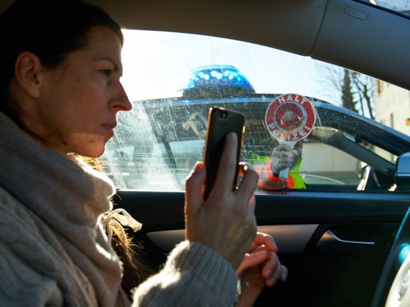 Eine Frau im Auto hält ein Smartphone in der Hand und wird von der Polizei angehalten.