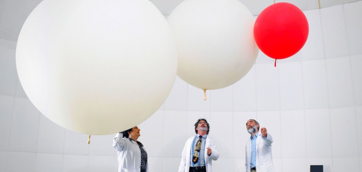 Menschen in Laborkitteln stehen unter drei Luftballons