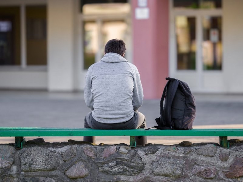 Ein Mann sitzt alleine auf einer Bank.