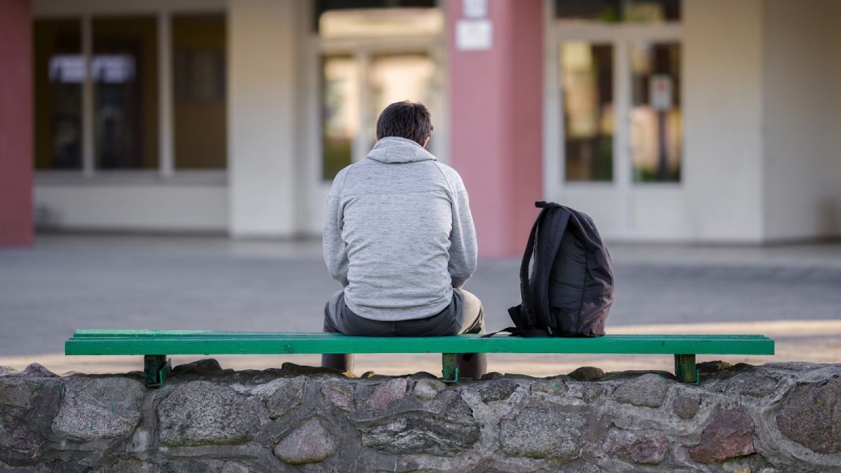 Ein Mann sitzt alleine auf einer Bank.