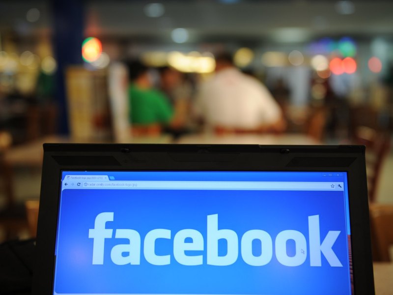 Facebook-Logo auf einem Bildschirm vor unscharfen Menschen im Hintergrund
