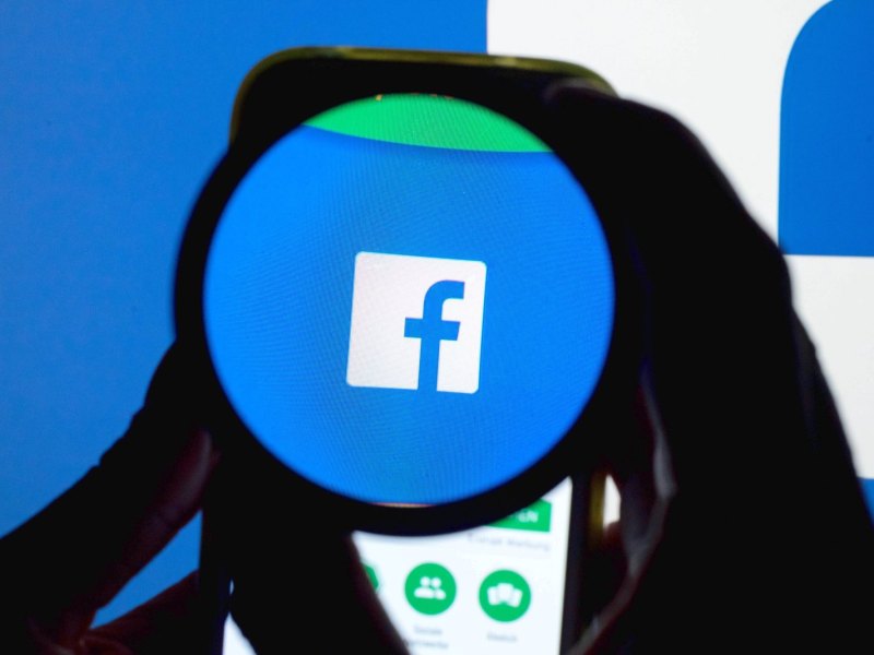 Das Icon der Social Media-Plattform Facebook ist auf einem Handy durch eine Linse zu sehen