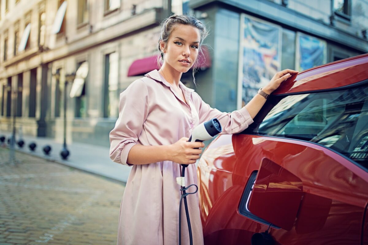 Eine Frau steht mit einem Ladegerät an einer Ladestation für ihr Elektroauto.