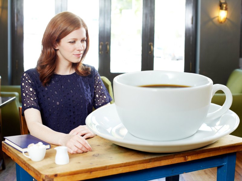 Frau mit übergroßer Tasse Kaffee am Tisch