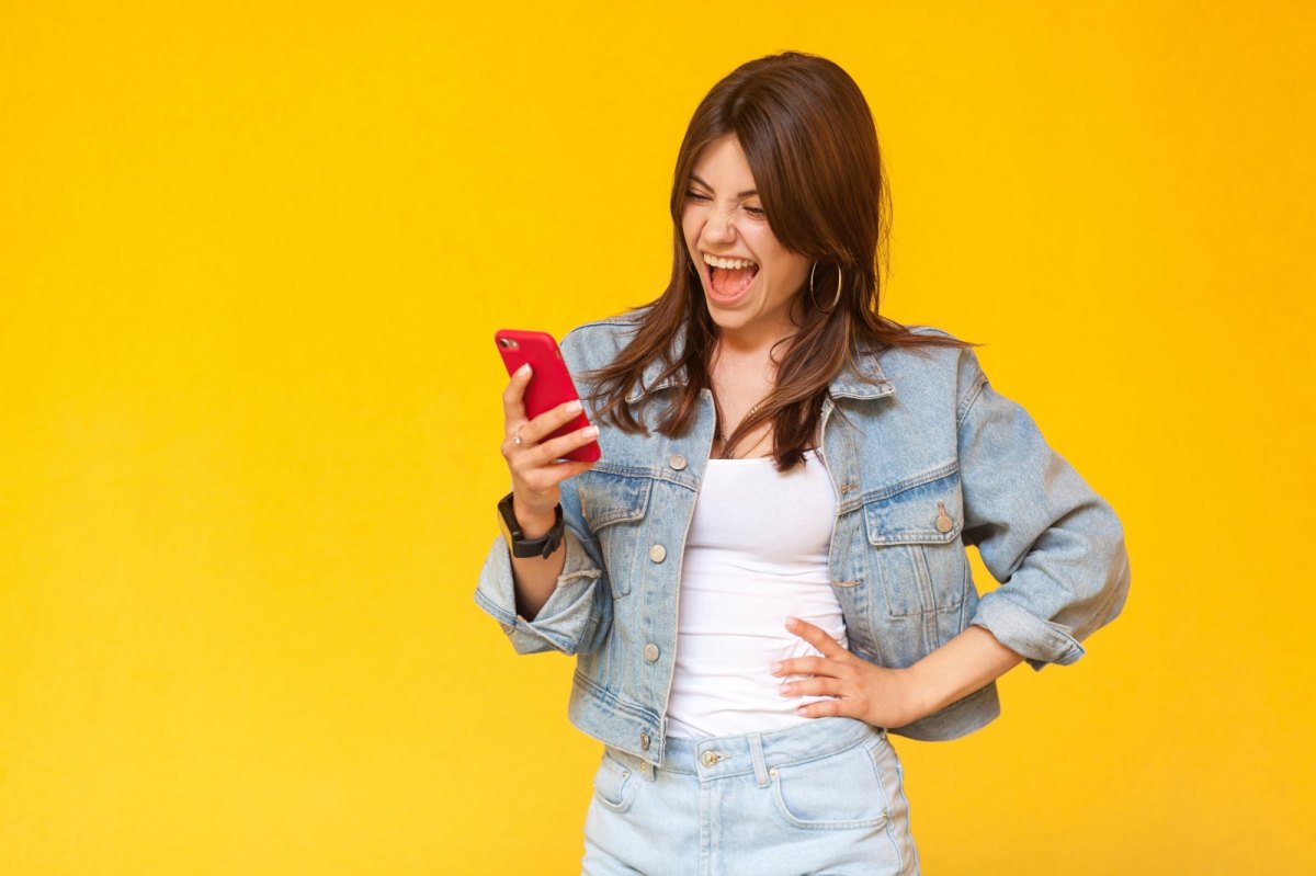 Frau blickt beeindruckt auf ihr Handy und stemmt eine Hand in die Hüfte.