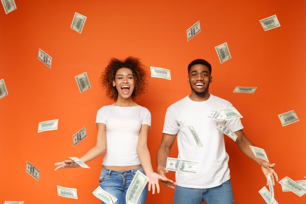Frau und Mann stehen vor orangenen Hintergrund und werfen fröhlich mit Geldscheinen um sich.