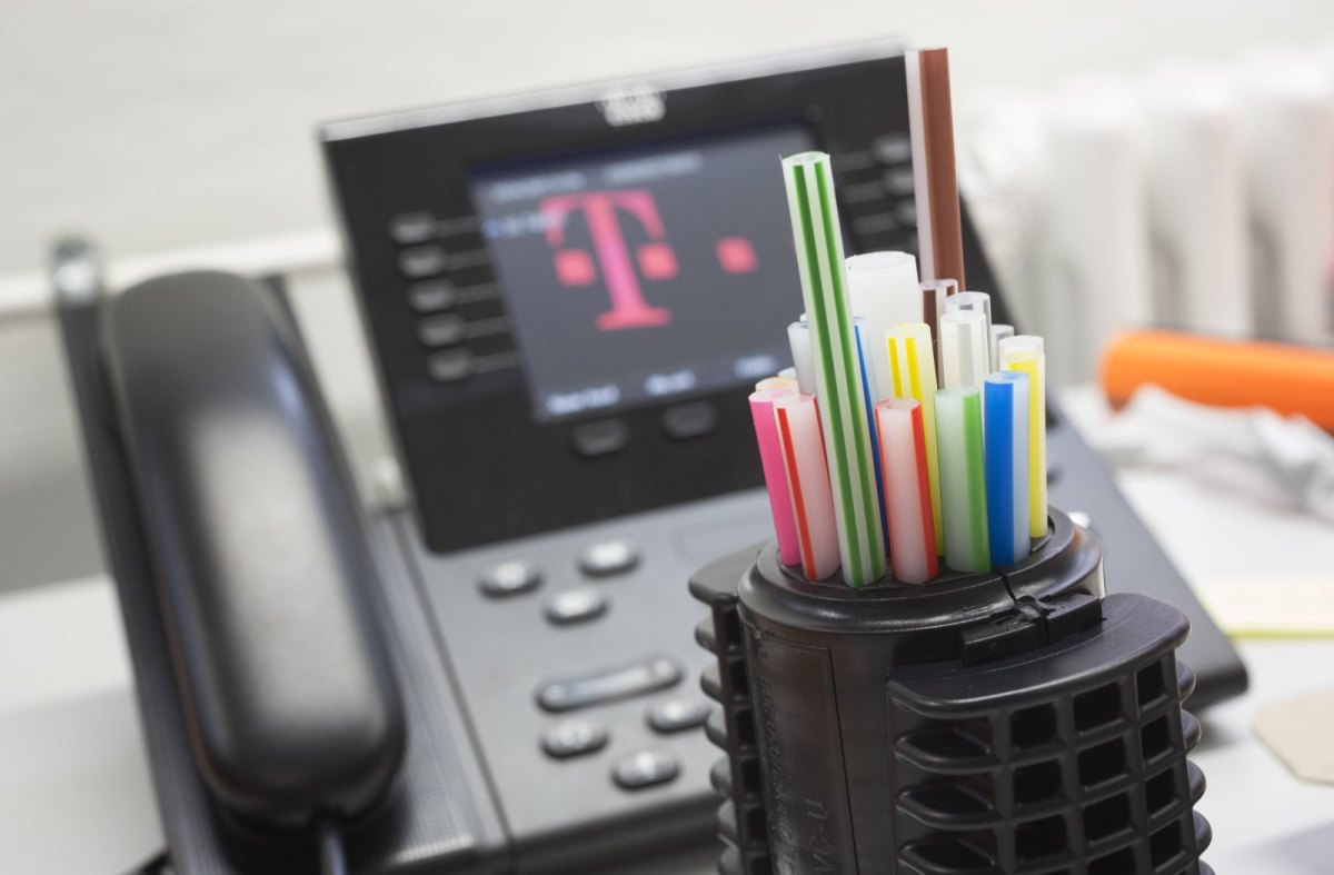 Leere Röhrchen für Glasfasern vor einem Telefon mit Telekom-Symbol auf dem Display