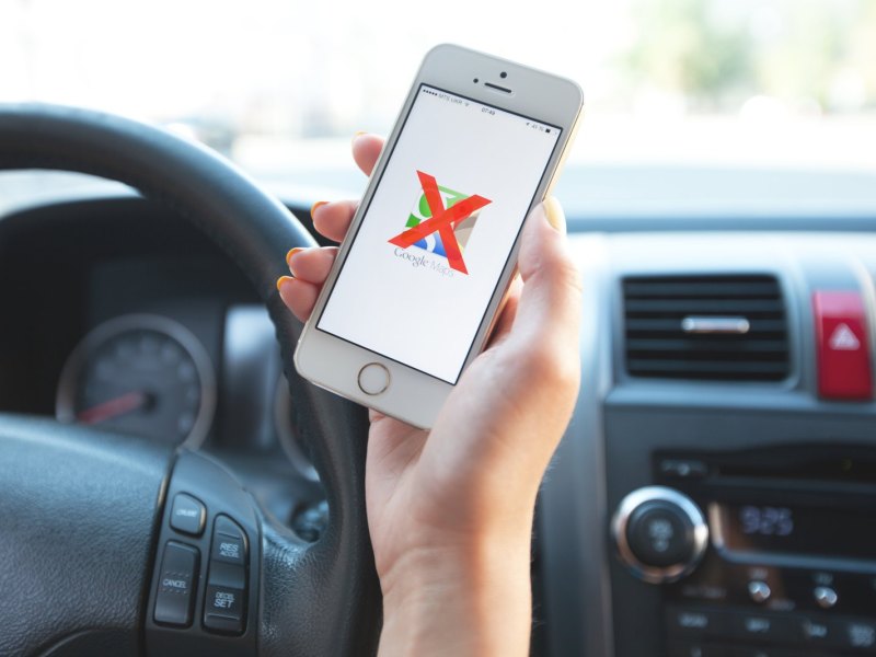 Frau hält Handy mit Google Maps-Logo im Auto in der Hand.