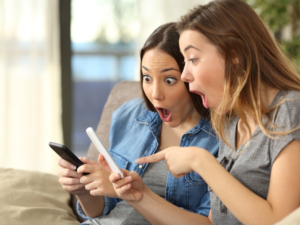 Zwei Frauen blicken erstaunt mit offenen Mündern auf ihre Handys.