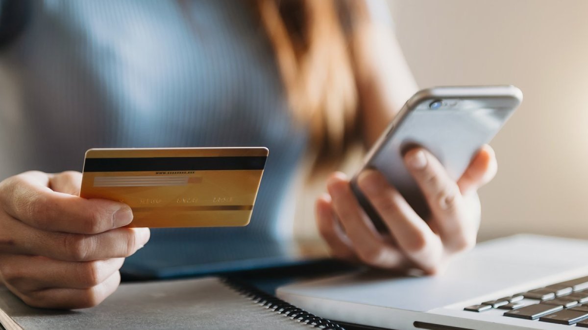 Frau hält ein Handy und eine Bankkarte in der Hand.