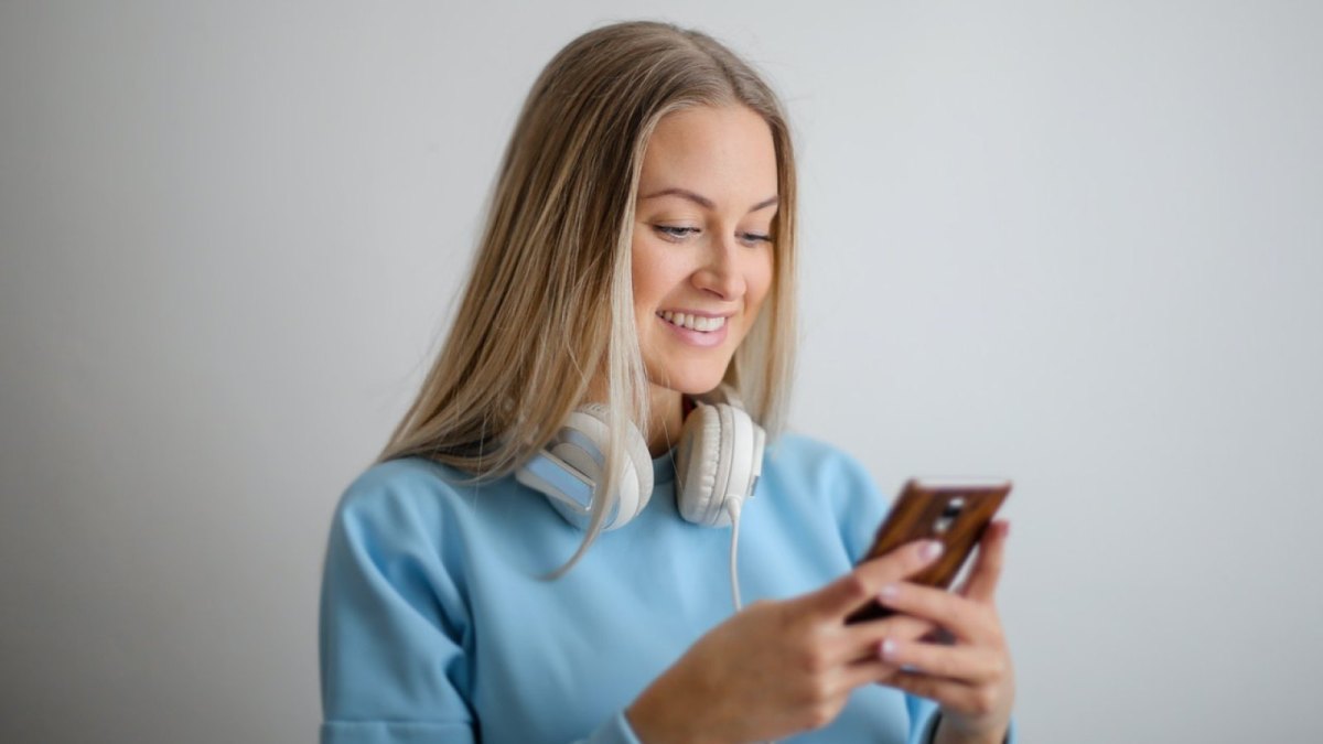 Eine Frau schaut auf ihr Handy und hat Over-Ear-Kopfhörer um ihren Hals gelegt.