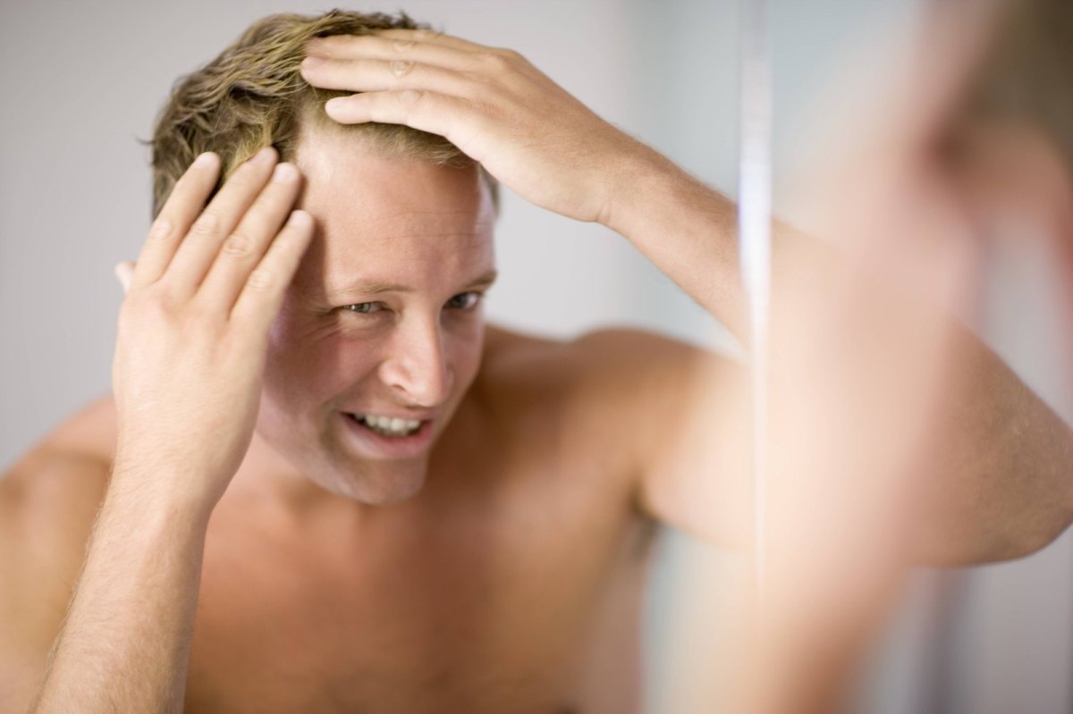 Mann schaut sich im Spiegel Haarausfall an