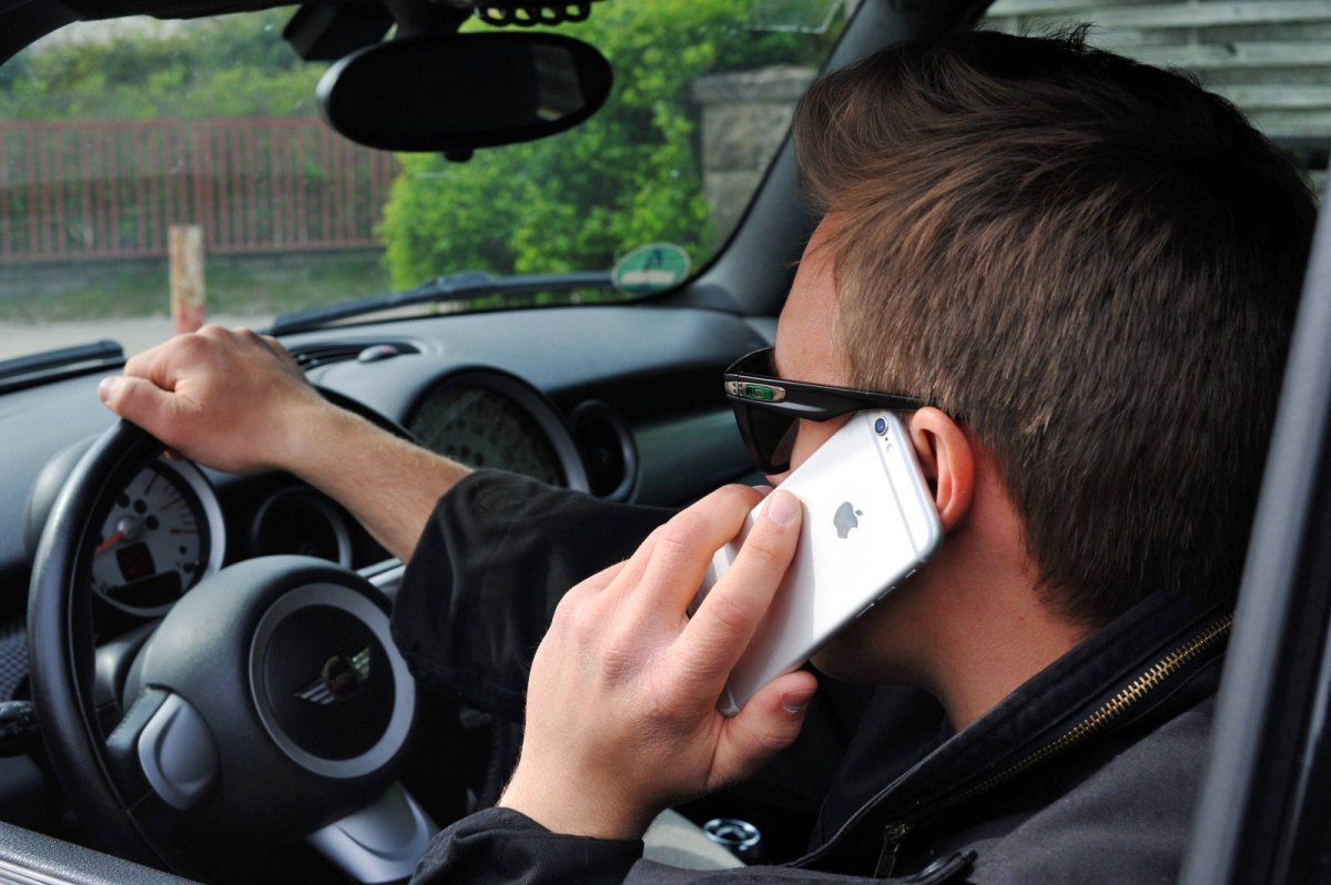 Mann mit Sonnenbrille telefoniert beim Autofahren mit seinem Handy.