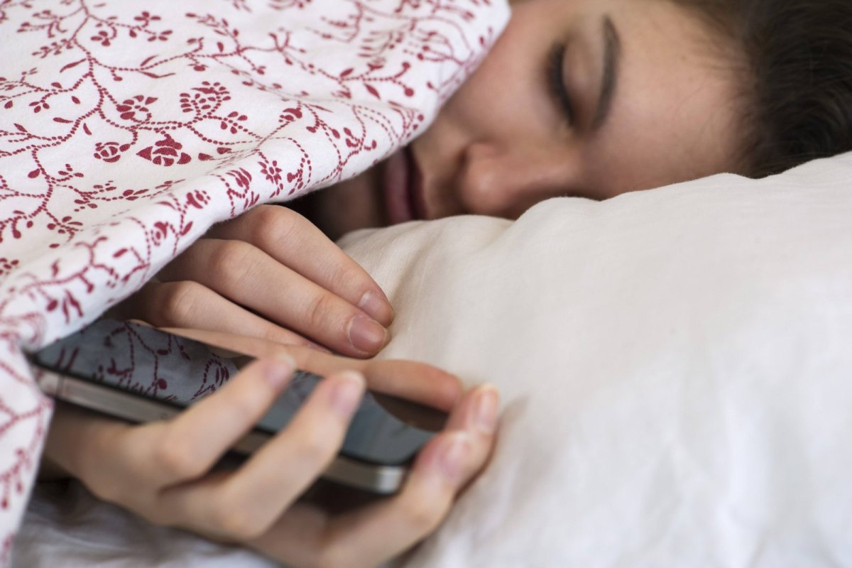 Frau im Bett mit Handy in der Hand