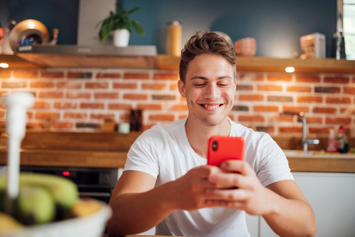 Junger blonder Mann mit Handy in der Küche.