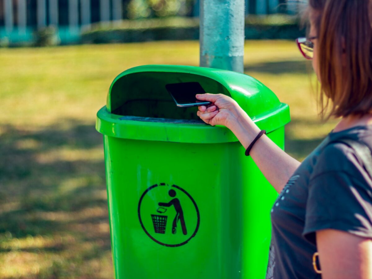Eine Frau wirft ein Handy in die Mülltonne.