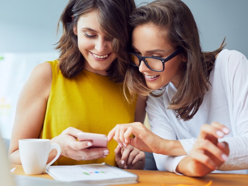 Zwei Frauen schauen neugierig auf ein Handy.