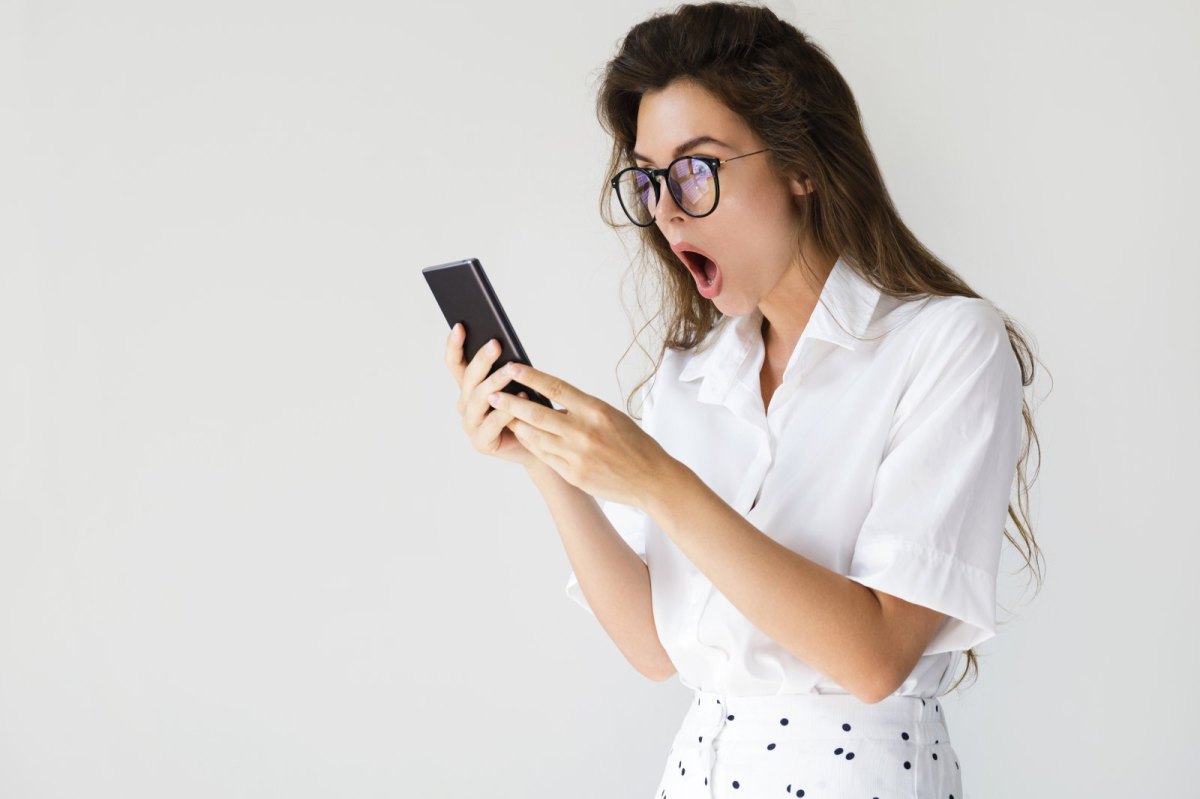 Frau mit Brille guckt geschockt auf ihr Handy.