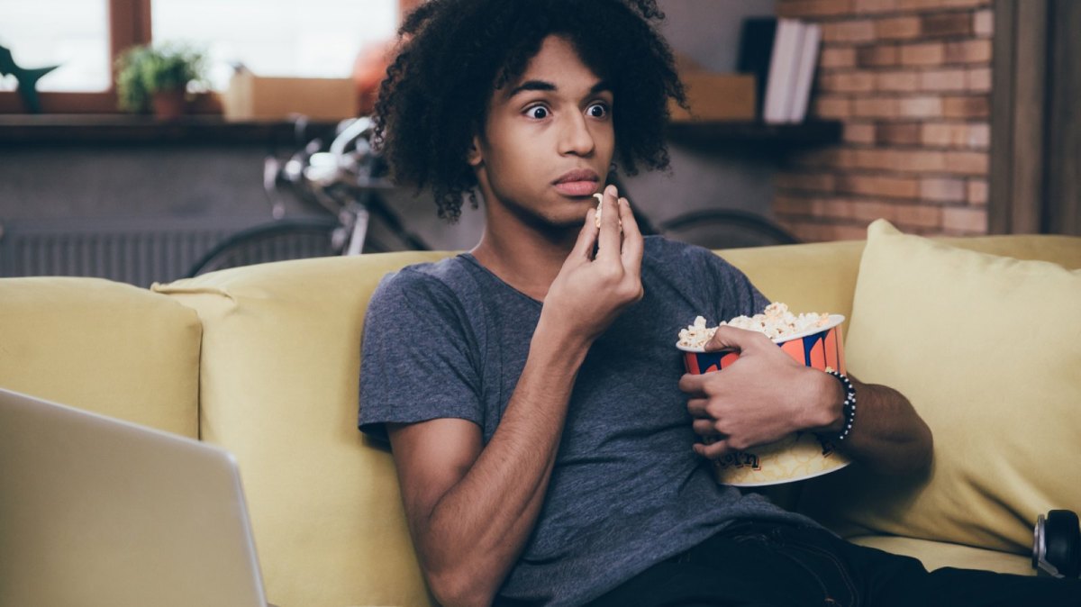 Mann sieht mit Popcorn in der Hand geschockt fern.