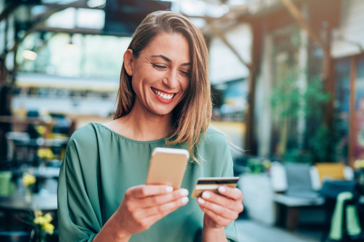 Frau mit Kreditkarte und Handy in der Hand lächelt.