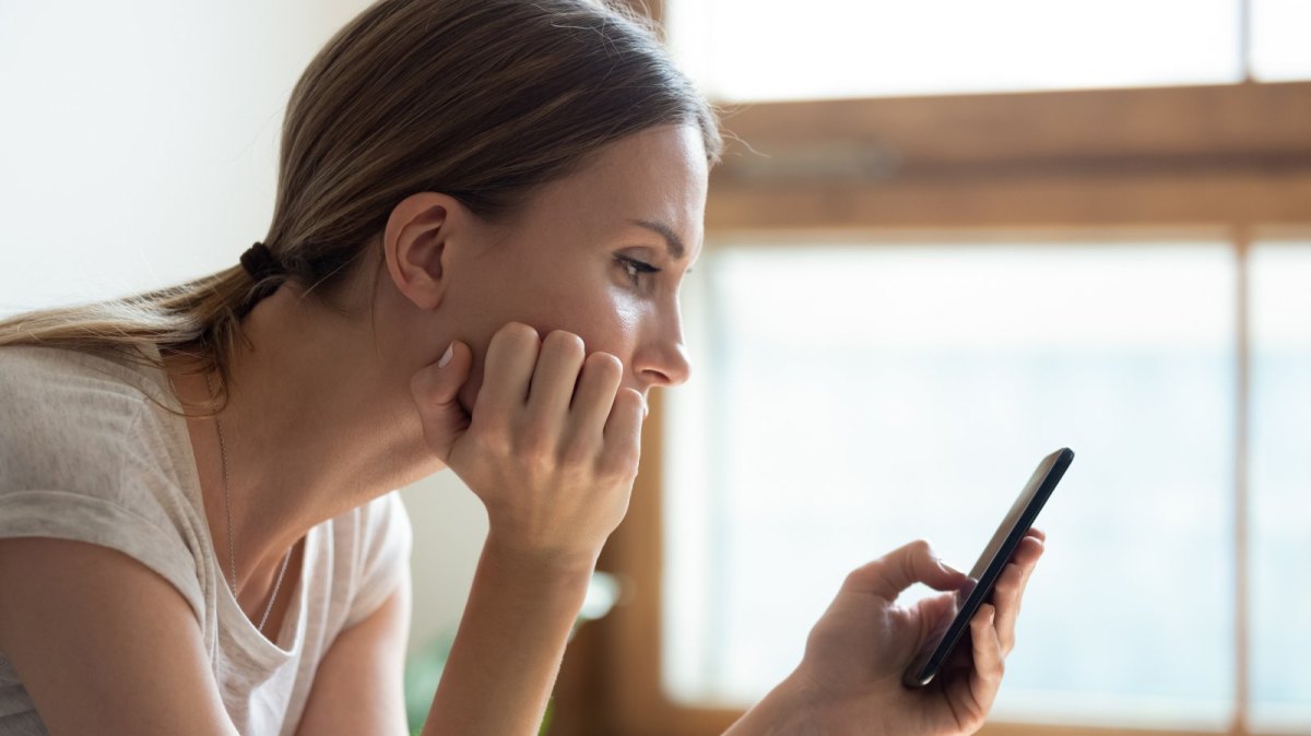 Frau schaut kritisch auf ihr Handy.