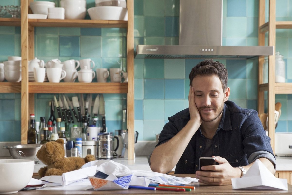 Ein Mann sitzt in einer Küche und schaut auf sein iPhone.