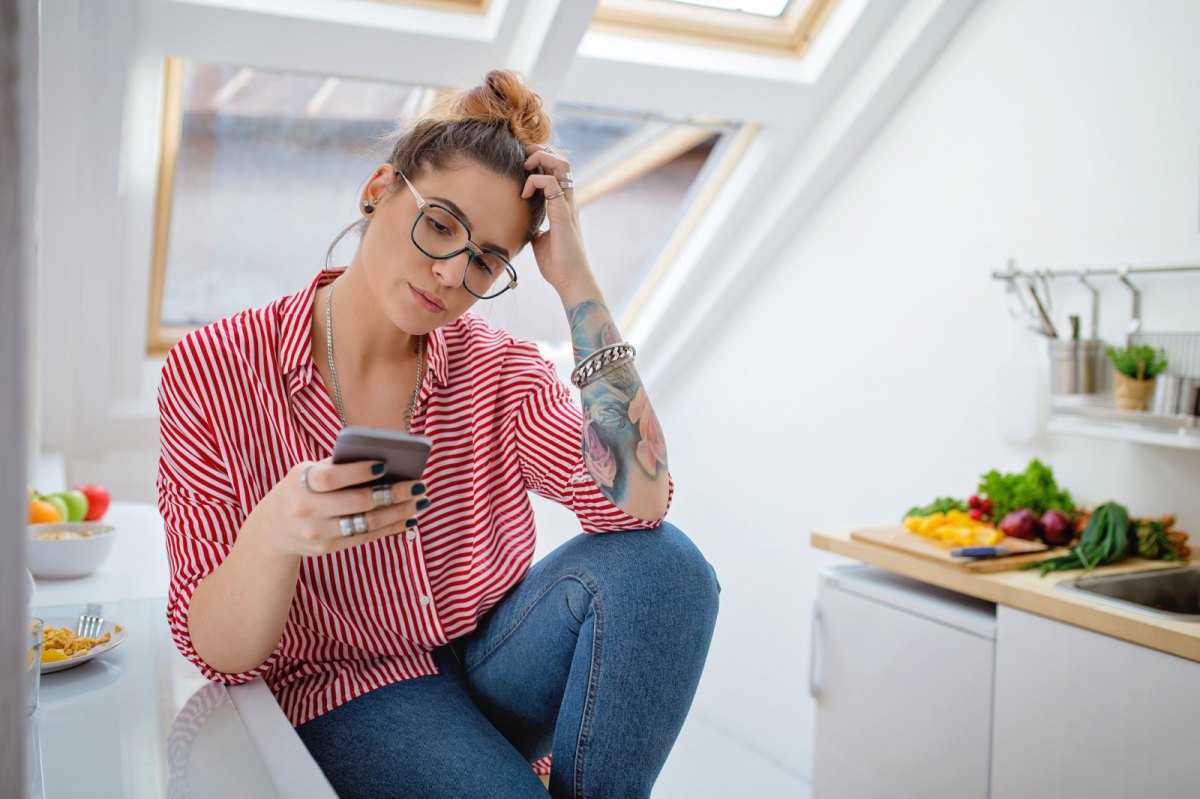 Frau schaut nachdenklich auf ihr Handy.