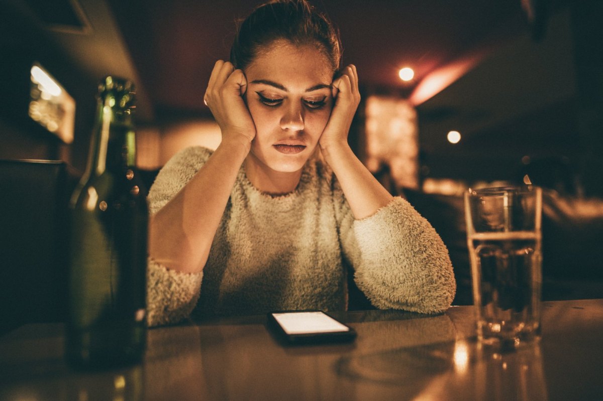 Frau schaut niedergeschlagen auf ihr Handy.