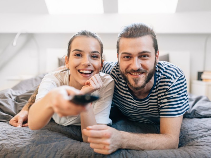 Frau und Mann liegen geimeinsam auf dem Bett und schauen fern.