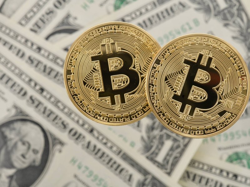 Zwei Bitcoin-Münzen liegen auf amerikanischen Dollar-Noten.