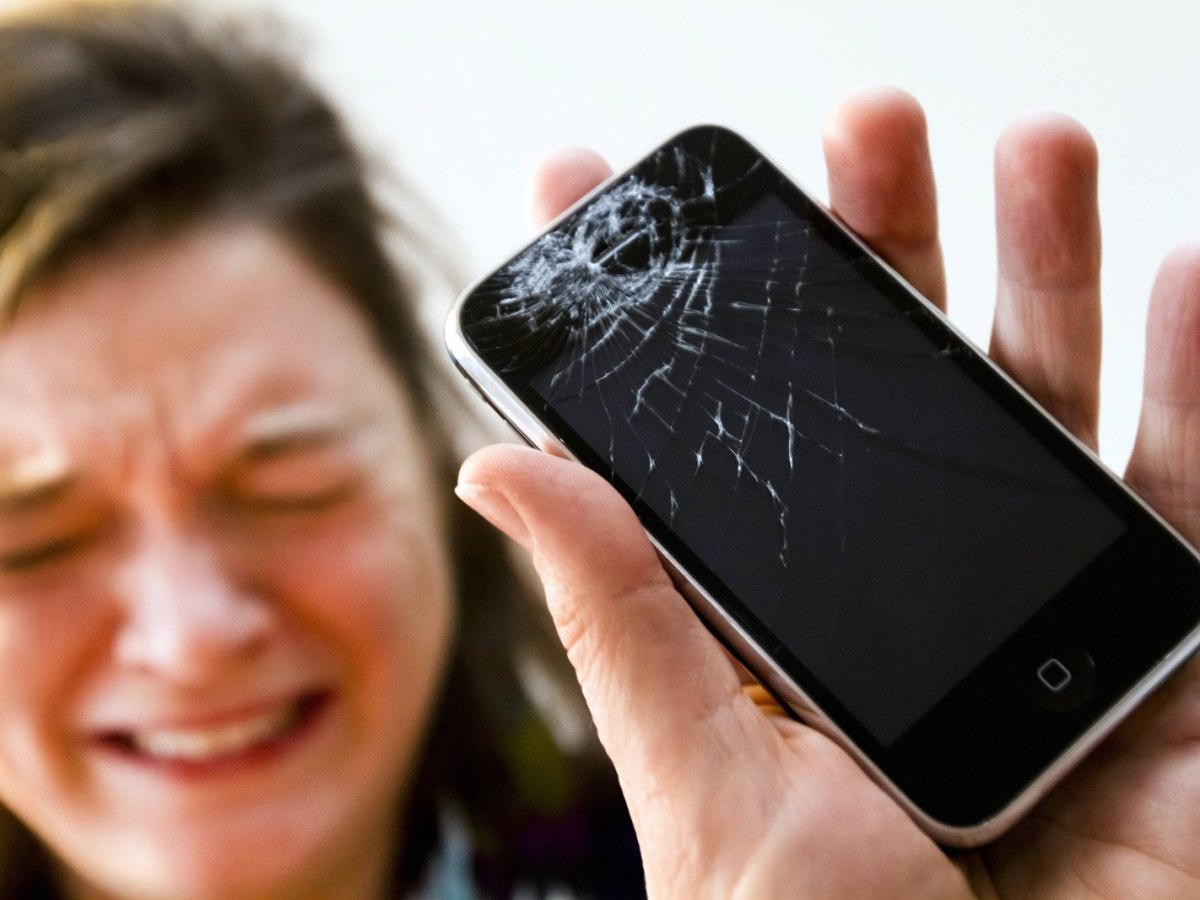 Eine Frau weint und hält ein kaputtes iPhone in der Hand.