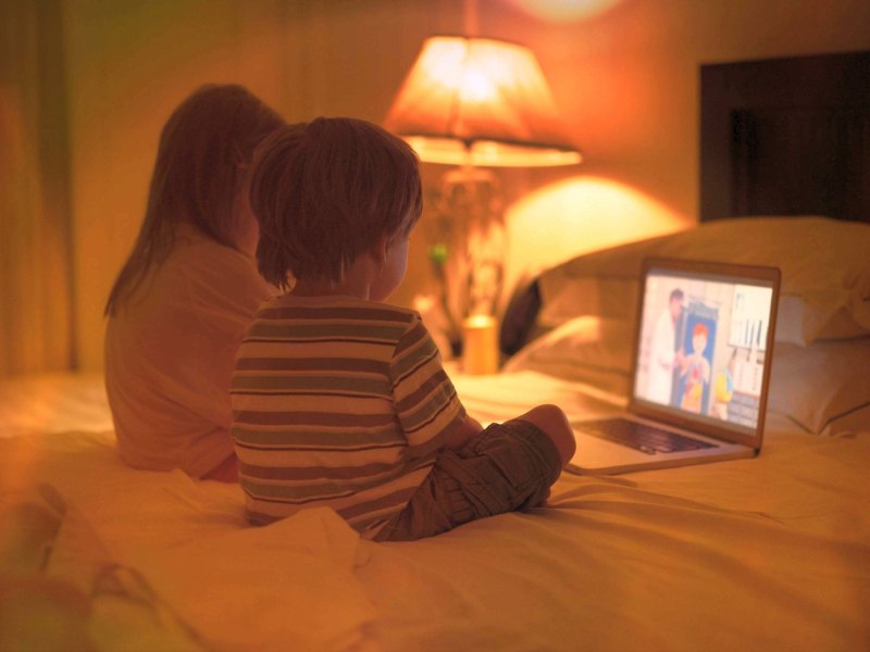 Mädchen und Junge sitzen vor einem Laptop und schauen einen zeichentrick.