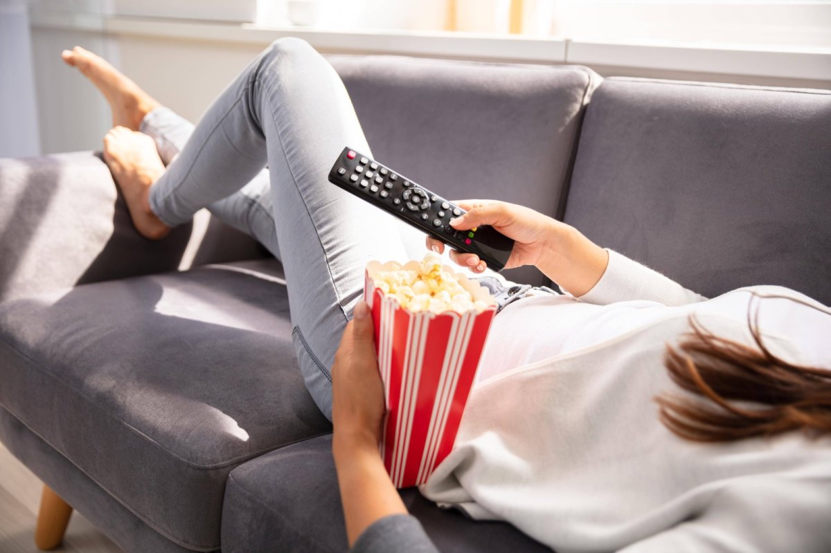 Person auf Couch mit Popcorn und Fernbedienung